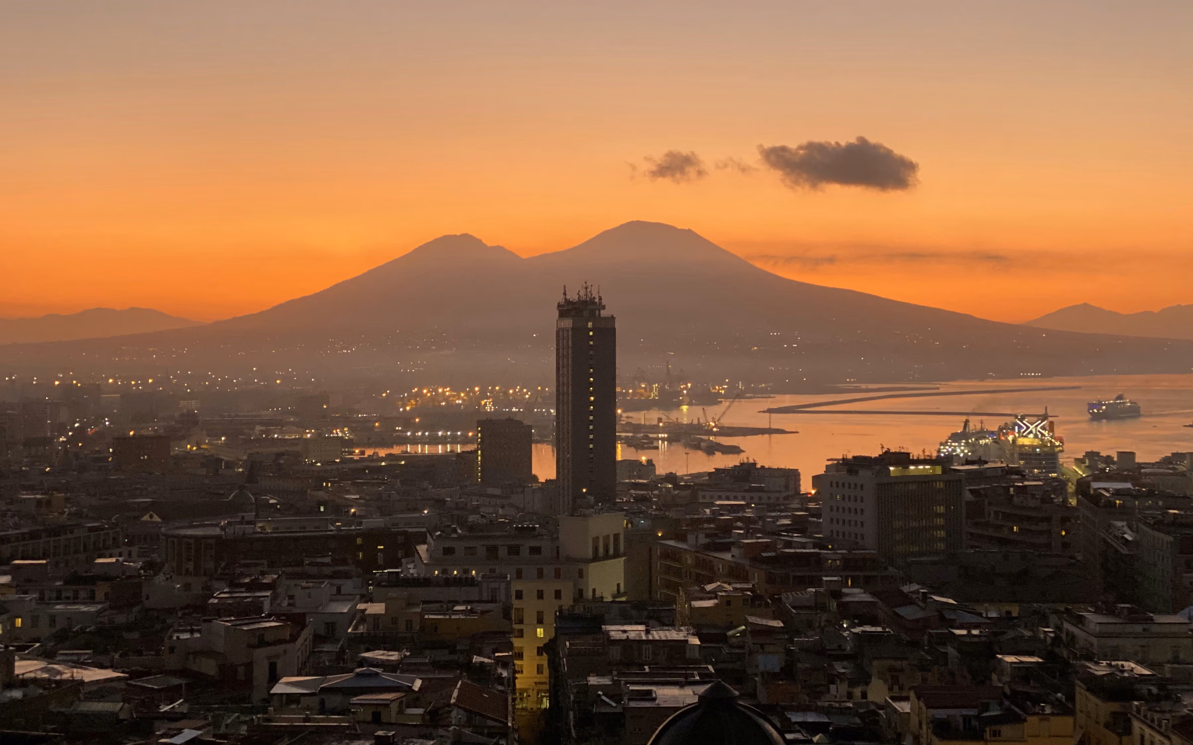 Napoli alla prima luce, con il profilo del Vesuvio in controluce sul golfo e le luci del porto ancora accese
